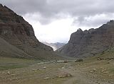 Tibet Kailash 08 Kora 10 View up Lha Chu Valley Entering the narrow valley on the western flank of Kailas, the place assigned to Amitabha, whose colour is red, he (the pilgrim) finds himself in a canyon of red rocks, the structure of which is so architectural in appearance that the pilgrim feels as if he is walking between rows of gigantic temples. They are adorned with elaborate rock-cornices, pillars, and ledges, and high above them there appears suddenly the dazzling ice-dome of Kailas.  Lama Anagarika Govinda: The Way of the White Clouds. You can just barely see Chuku Gompa on the hill to the left of the V in the valley.